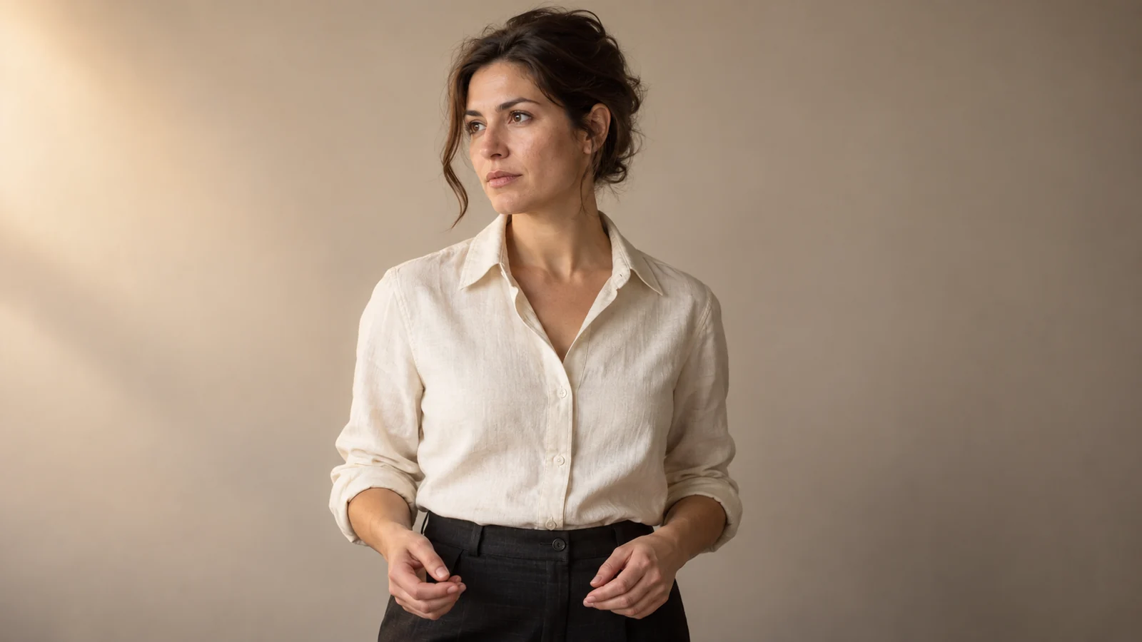 Référence de l’horlogère fictive : cheveux bruns relevés, chemise écrue et lumière chaude venant de la gauche.
